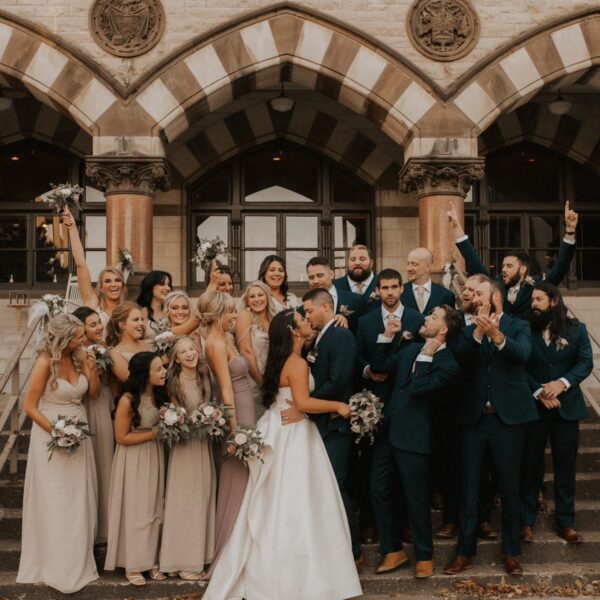 bride and groom kissing surrounded by cheering wedding party