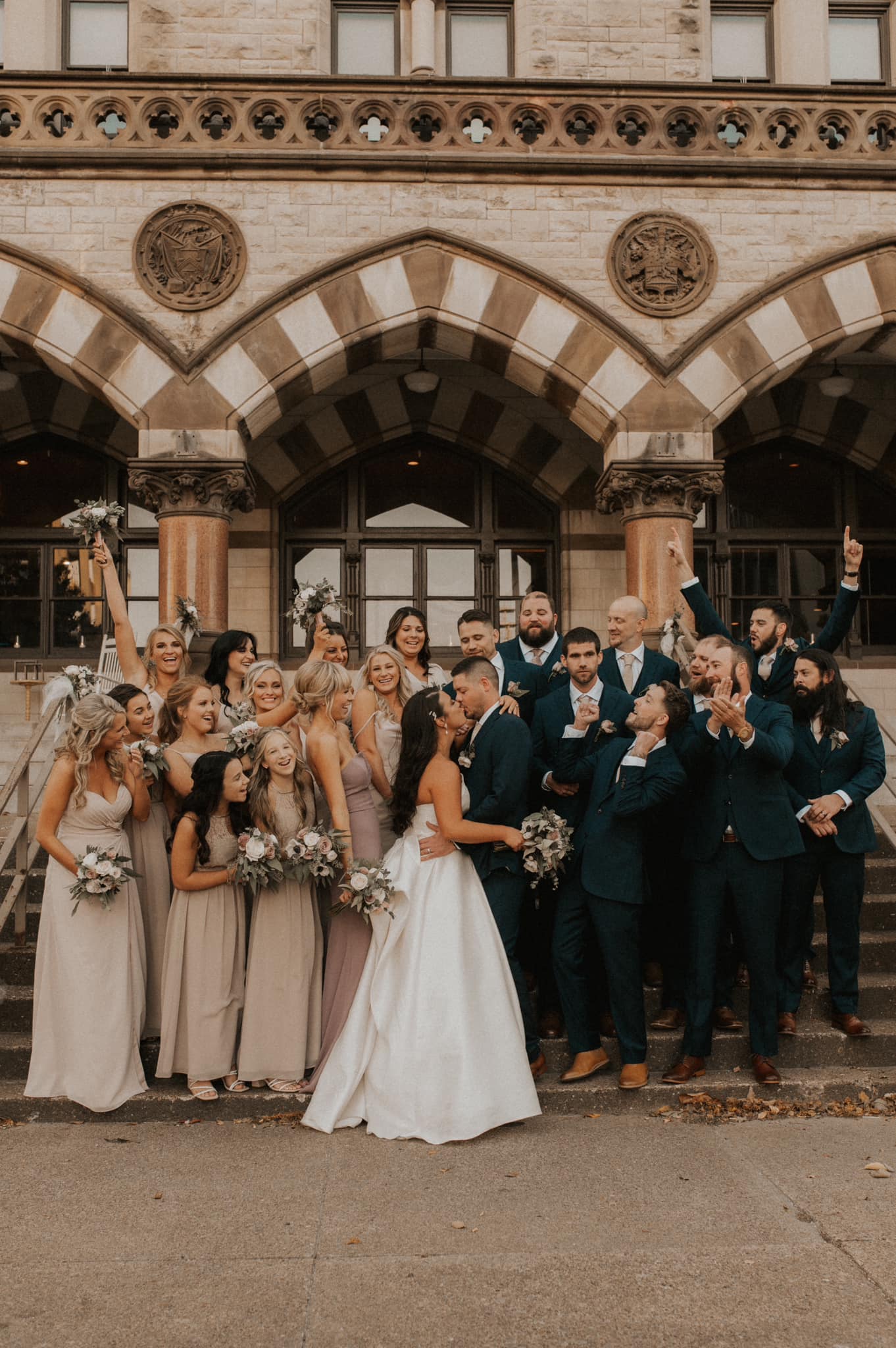bride and groom kissing surrounded by cheering wedding party
